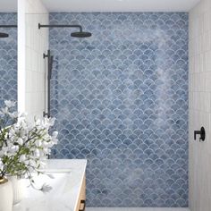 a bathroom with blue tiles on the wall and white counter tops, along with a vase filled with flowers