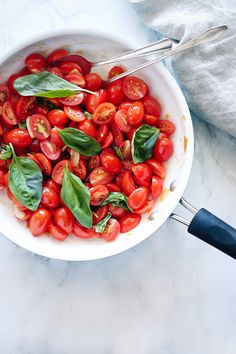 a white bowl filled with tomatoes and basil on top of a marble counter next to a black spatula