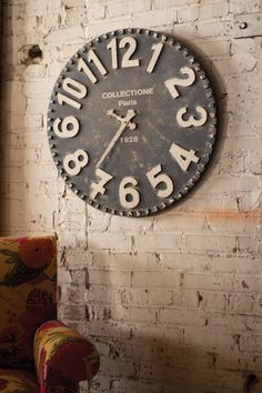 an old clock is on the wall next to a chair and armrests in front of a brick wall