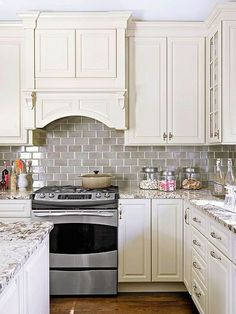 a kitchen with white cabinets and marble counter tops, an oven and stove top in the center