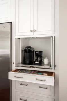 a kitchen with white cupboards and drawers has a coffee maker on the bottom shelf