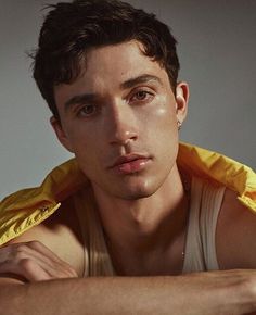 a young man wearing a yellow jacket and looking at the camera with his hand on his chest