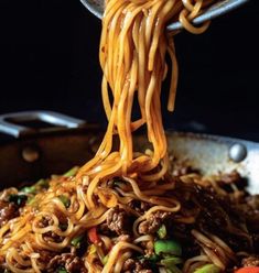 noodles being cooked in a wok with chopsticks over it and vegetables on the side