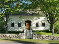 a white house with a wooden door in the front yard surrounded by trees and grass