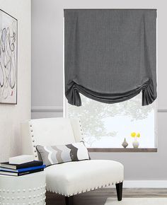 a white chair sitting next to a window covered in roman shades and pillows on top of a rug