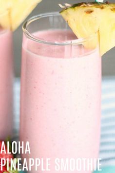 two glasses filled with pink smoothie next to strawberries and a pineapple on the side