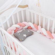 a white crib with a pink and grey pillow in it