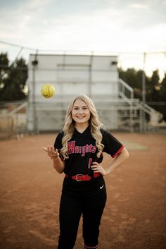 a softball player is throwing a ball in the air while standing on a dirt field