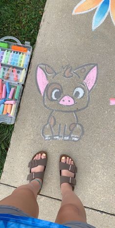 a person standing next to a sidewalk with chalk drawings on it and crayons in the background