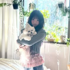 a young woman holding a teddy bear in her arms while standing next to a window