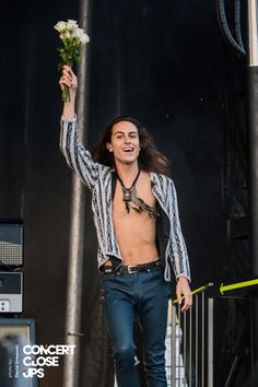 a man with no shirt on is holding flowers in his hand while walking down the stage