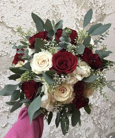 a bridal bouquet with red and white flowers on a pink glove against a textured wall