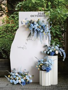 blue flowers and greenery are on display in front of a sign that says october