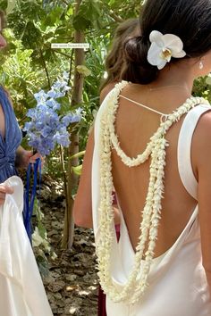 two women standing next to each other in front of trees and bushes with flowers on them