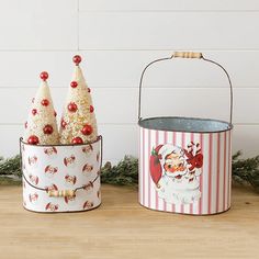 two tin canisters decorated with christmas trees and santa clause decorations, one is holding a candy cane