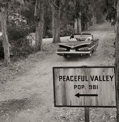 an old car driving down a dirt road next to a sign