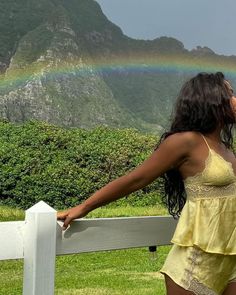 a woman leaning on a fence with a rainbow in the background