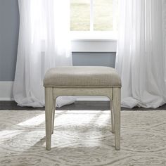 a white bench sitting in front of a window next to a rug and curtained wall