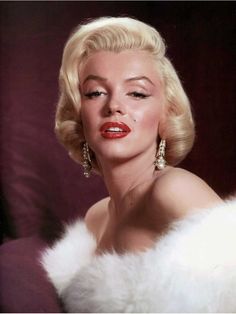 a woman with blonde hair and big earrings posing for a photo in front of a dark background