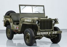 an old green jeep is parked in a garage