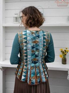 a woman standing in front of a shelf wearing a blue and brown top with an open back