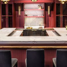 a kitchen with red cabinets and marble counter tops, along with black bar stools