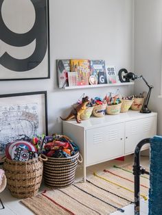 a room filled with lots of toys and baskets on top of a white dresser next to a window