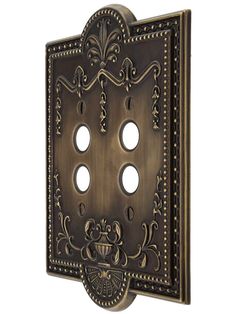 an ornately designed metal outlet cover with four holes in the center and two on each side