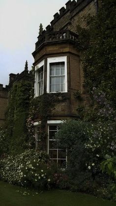 an old building with ivy growing on it's side and flowers in the foreground