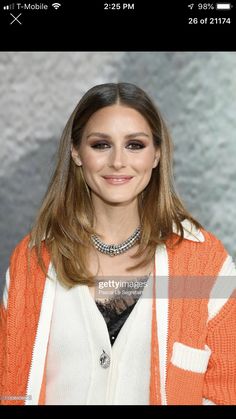 a woman in an orange and white cardigan smiles at the camera