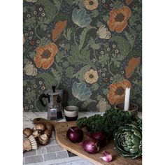 an assortment of vegetables on a wooden cutting board next to a wallpapered wall