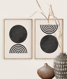 two black and white art prints hanging on a wall next to vases with dry grass