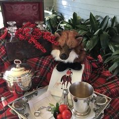 a stuffed fox sitting on top of a table next to silver cups and saucers