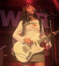 a woman holding a white guitar while standing in front of a microphone