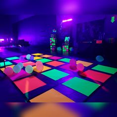 an indoor dance floor is lit up with colored lights and balls in the middle of it