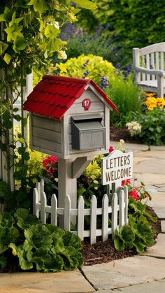 a mailbox with a red roof is in the middle of a flower bed and fence