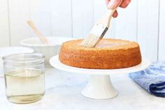 someone using a paint brush to decorate a cake on a white pedestal with blue napkins