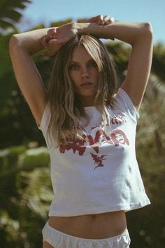 a woman in white shirt and shorts holding her hands up to her head with palm trees in the background