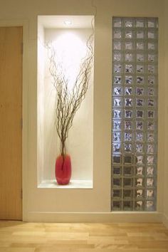 a vase with some branches in it sitting on a wooden floor next to a glass block wall