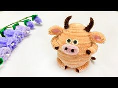 a small stuffed animal sitting next to purple flowers on a white surface with green stems in the foreground