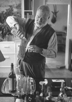 an old man standing in front of a counter filled with bottles and glasses