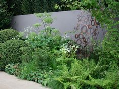 a garden with lots of green plants next to a large metal sculpture in the middle