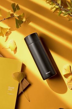 thermos are placed next to some leaves on a yellow surface with other items