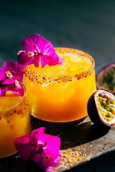 two glasses filled with orange juice and garnished with purple flowers on a metal tray