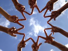 several hands making a star shape with their fingers in the air against a blue sky