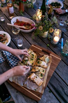 people are sitting at a table with food and drinks on the wooden table, while one person is placing slices of bread in front of them