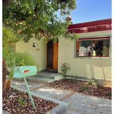 a green mailbox sitting in front of a house next to a tree and bushes