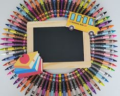 there are many different colored crayons arranged around a blackboard with a school bus on it