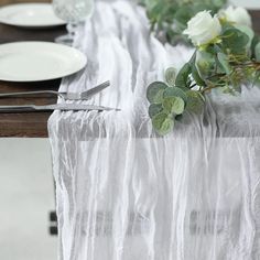 the table is set with white plates and silverware, flowers and greenery on it