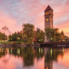 a large clock tower towering over a lake at dusk with lights reflecting in the water